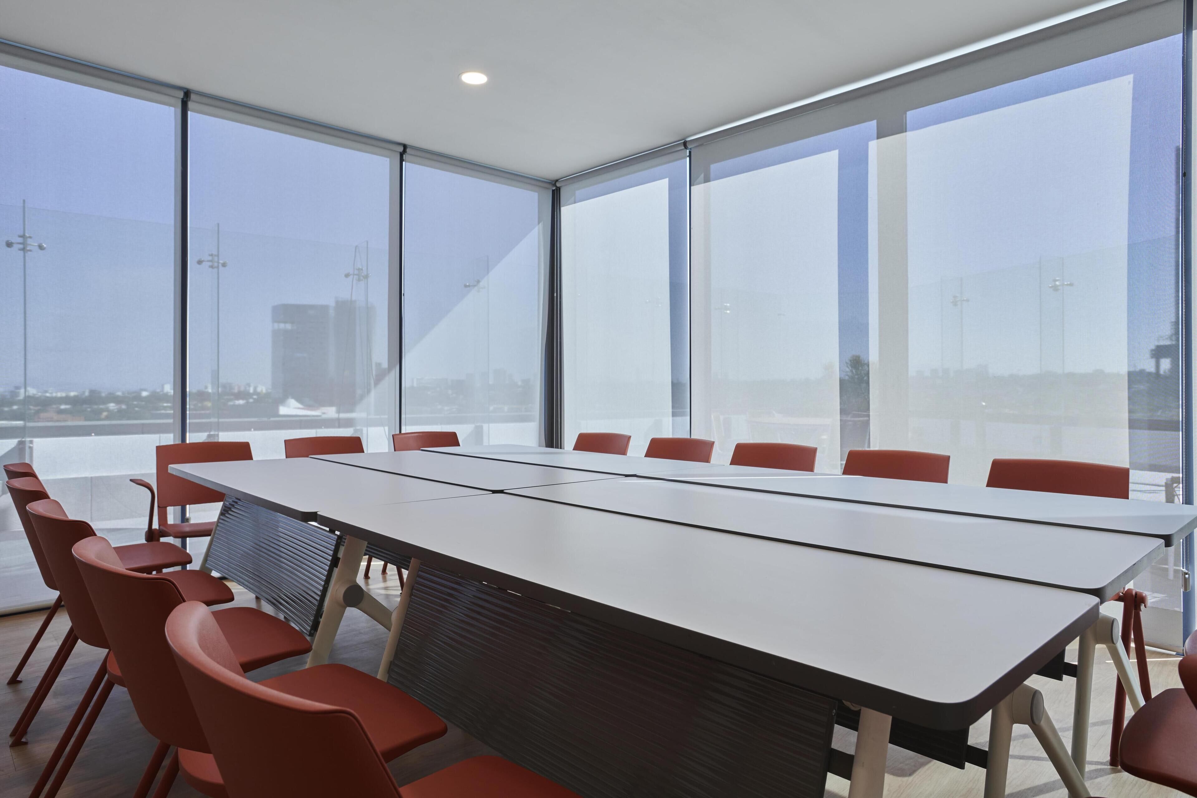 A conference room with a long table and red chairs, large windows with a city view, and a modern design.