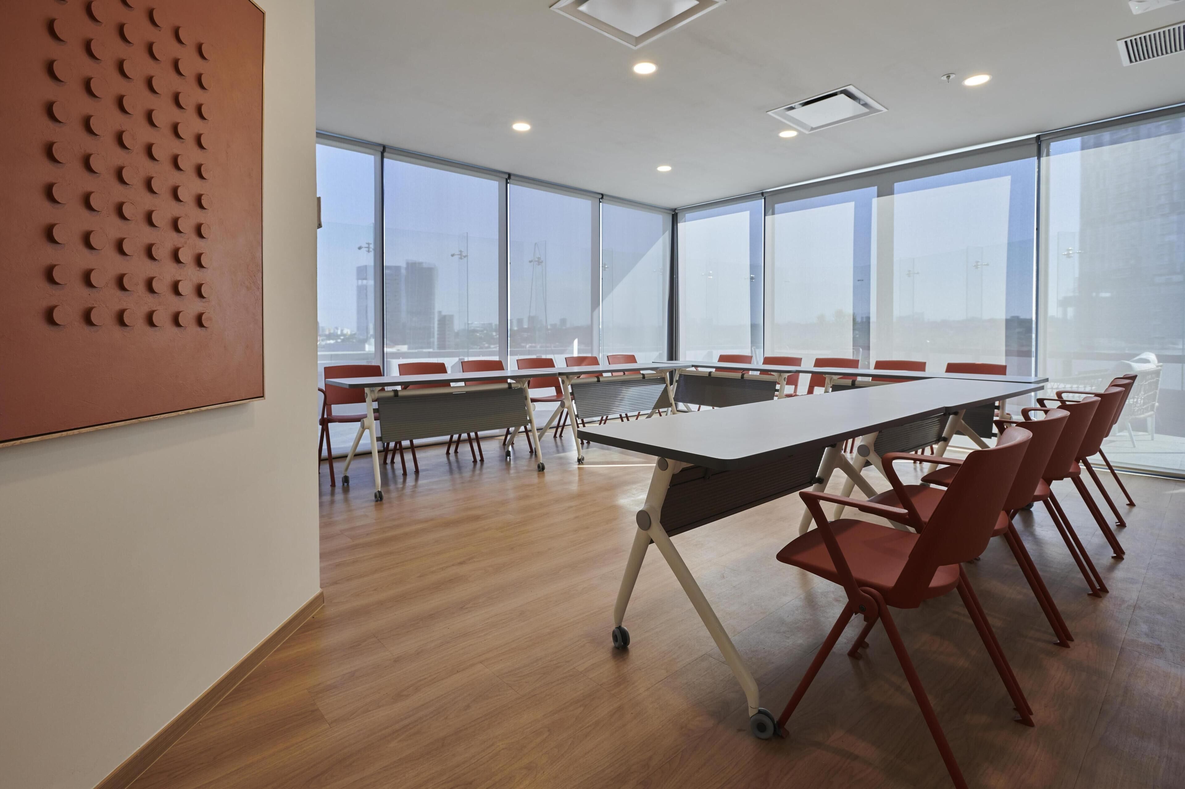 Una sala conferenze con un lungo tavolo e sedie rosse, ampie finestre e vista sulla città.