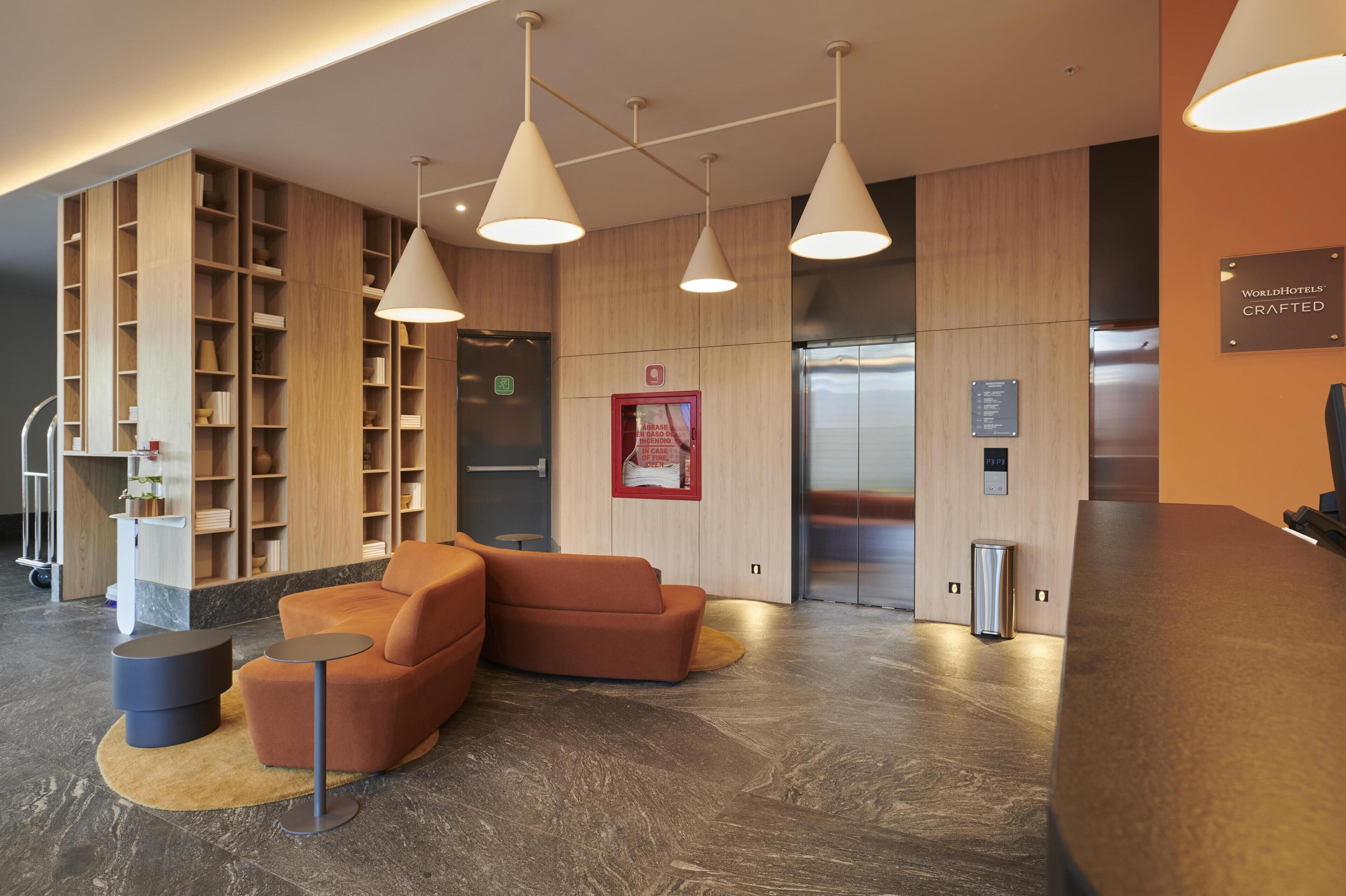 A modern lobby with a wooden bookshelf, a seating area with orange sofas, and a reception desk.