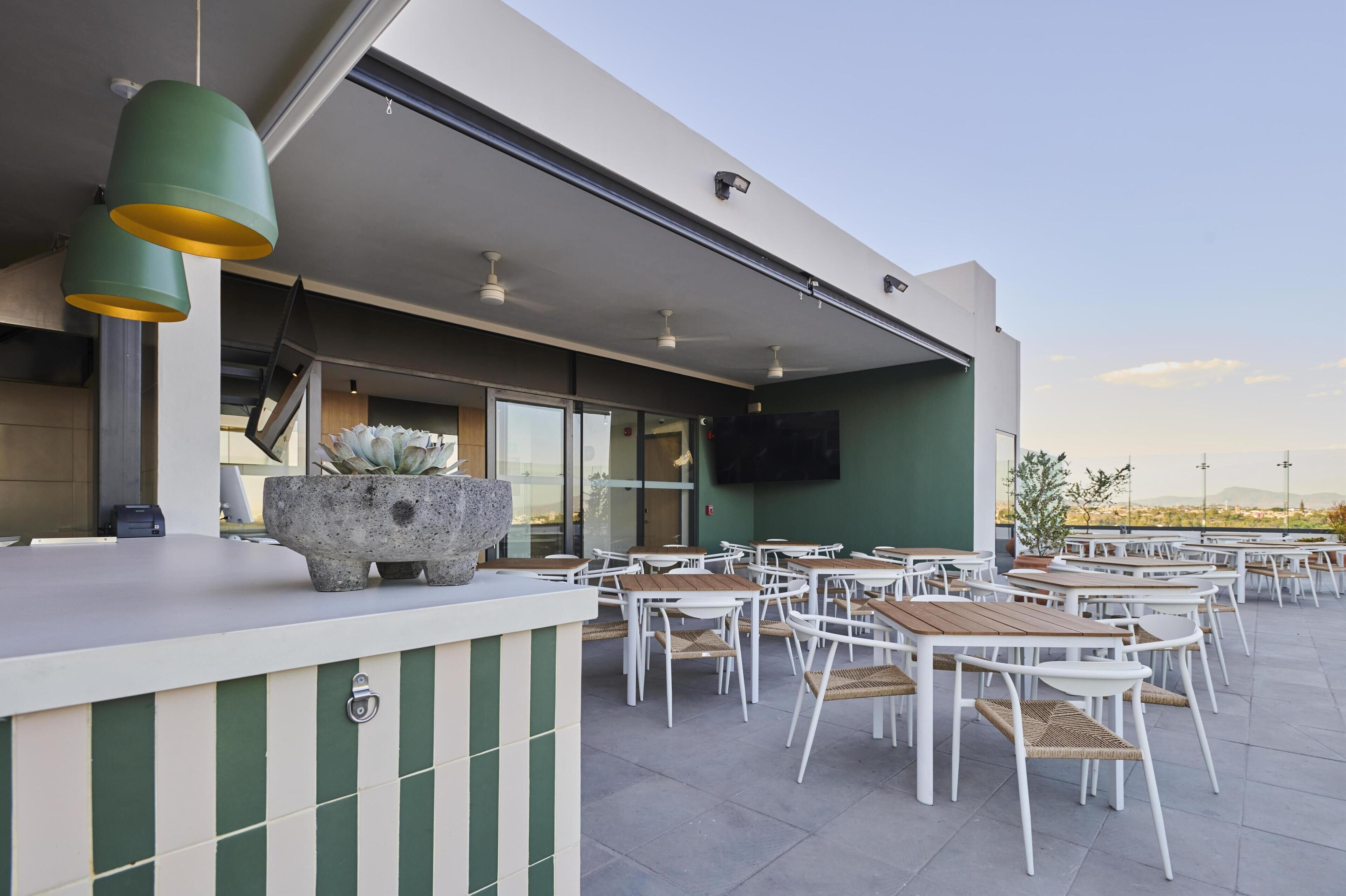 An outdoor seating area with tables and chairs, a stone planter, and a flat-screen TV mounted on the wall.