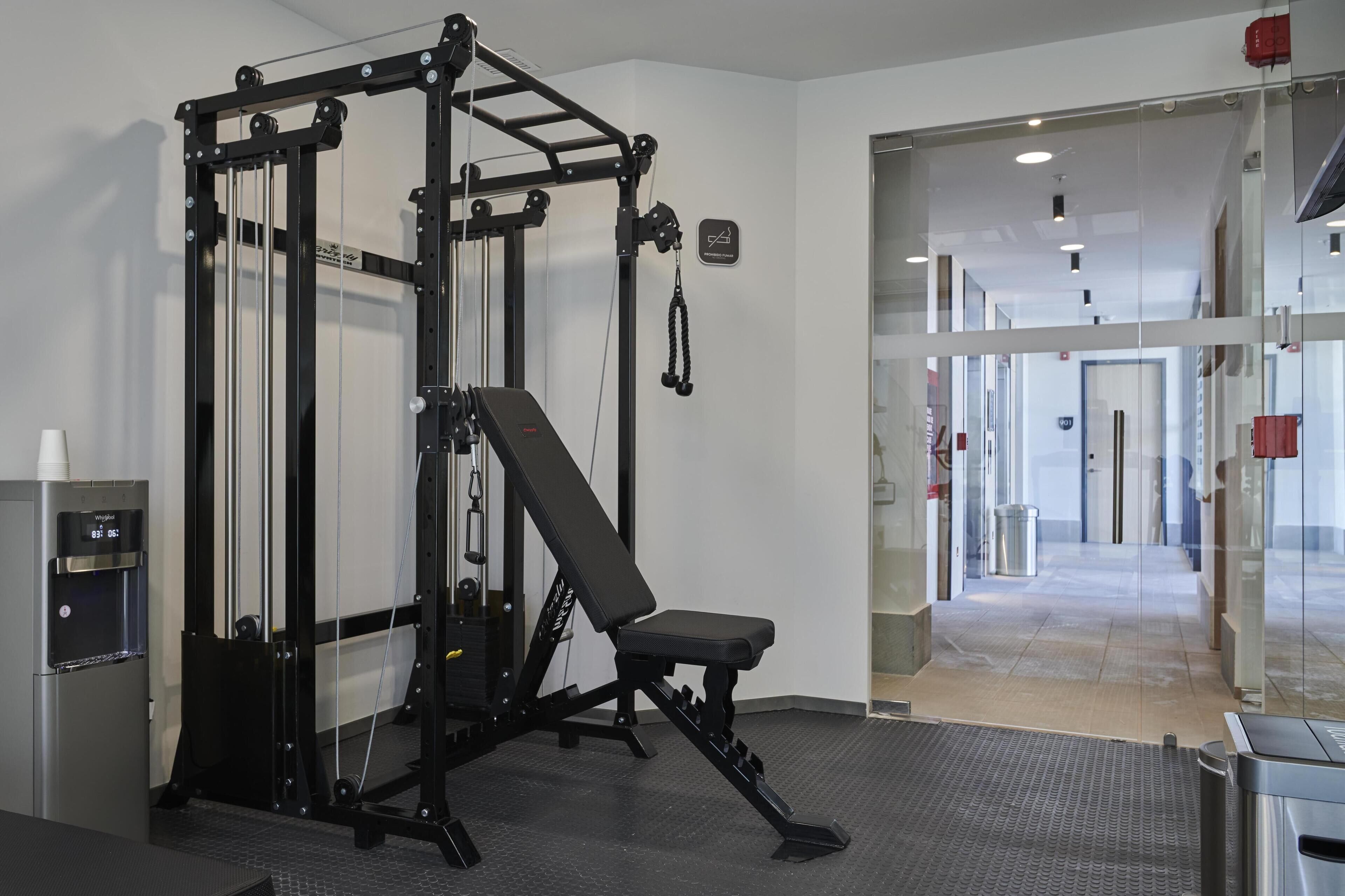 Uma academia com banco de musculação, suporte para agachamento e bebedouro.