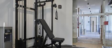 Uma academia com banco de musculação, suporte para agachamento e bebedouro.