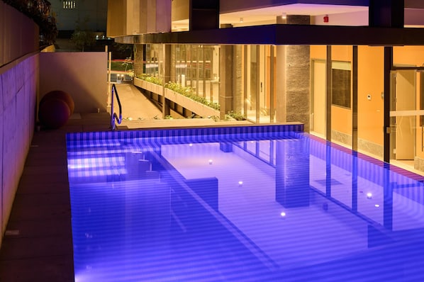 A modern indoor pool with clear water, surrounded by a wooden deck and glass walls.