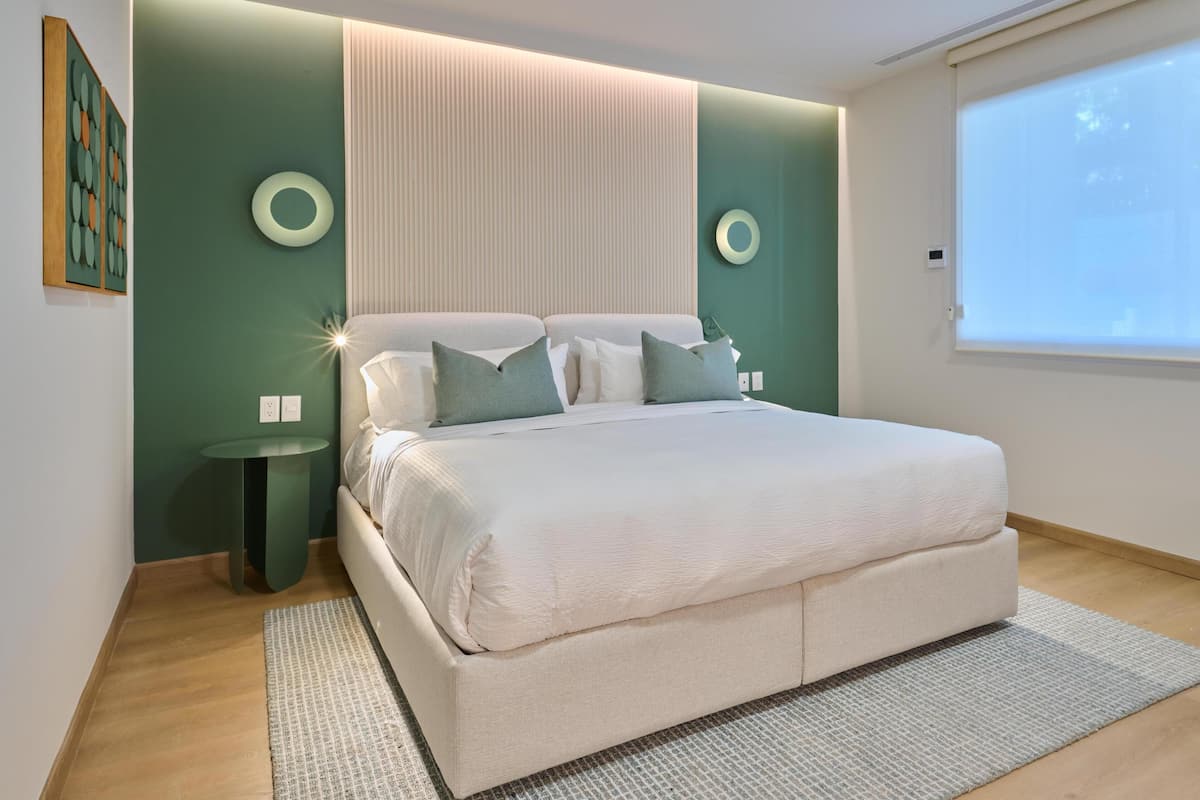 Quarto moderno com uma cama grande, mesa de cabeceira e luminária fixada na parede.