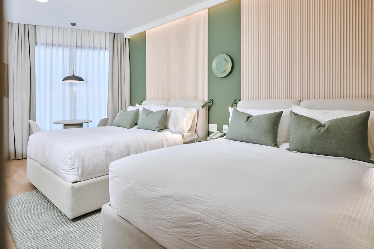 Quarto de hotel com duas camas, uma mesinha e um abajur.
