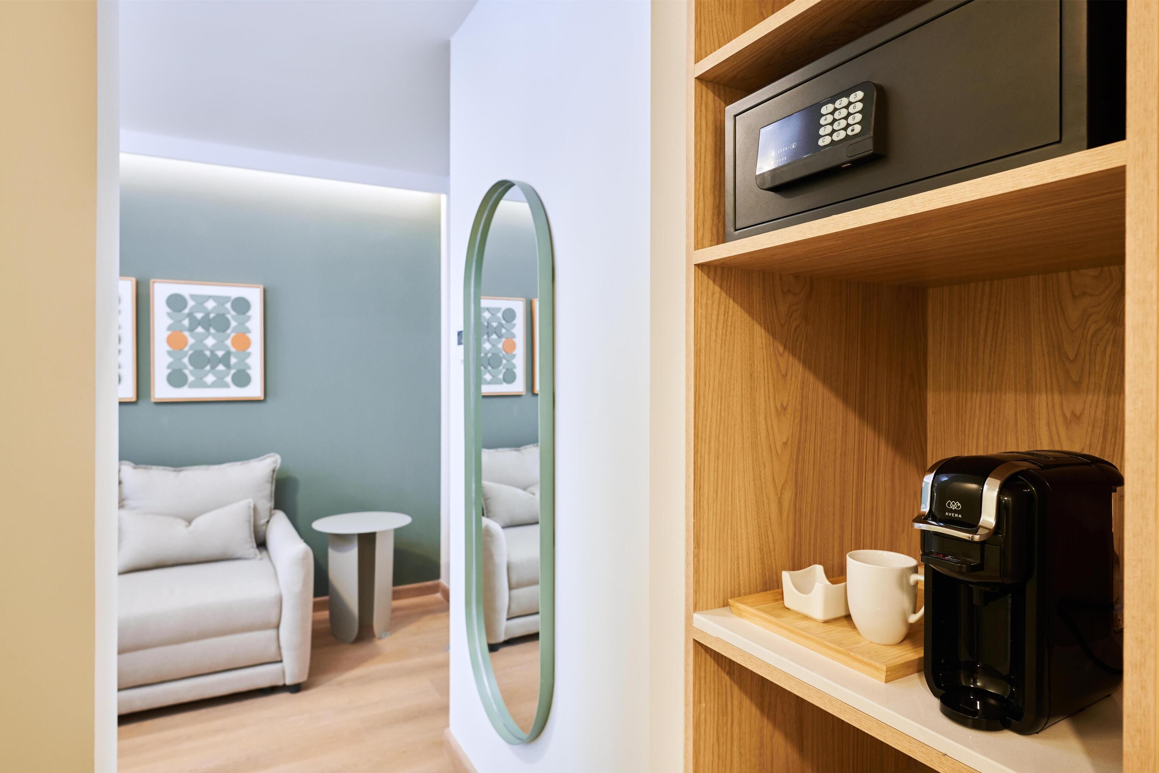 A modern hotel room with a sofa, a small round table, a coffee machine, and a shelf with a microwave.