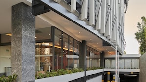 A modern building with a glass facade, a central staircase, and a landscaped area with plants. - WorldHotels Guadalajara Zona Andares (Zapopan)