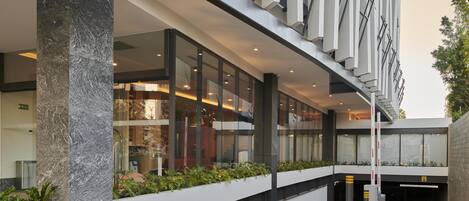 Un edificio moderno con fachada de vidrio, una escalera central y un área ajardinada con plantas.