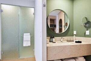 Un baño con puerta de cristal, lavabo con espejo y perchero para toallas.