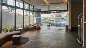 Eine moderne Lobby mit großen Fenstern, einer Sitzecke mit runden Hocker und Blick auf die Straße.