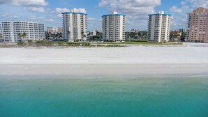 Ein Strandhotel mit mehreren Hochhäusern, einem Sandstrand und klarem türkisblauem Wasser.