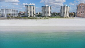 Ein Strandhotel mit mehreren Hochhäusern, einem Sandstrand und klarem türkisblauem Wasser.