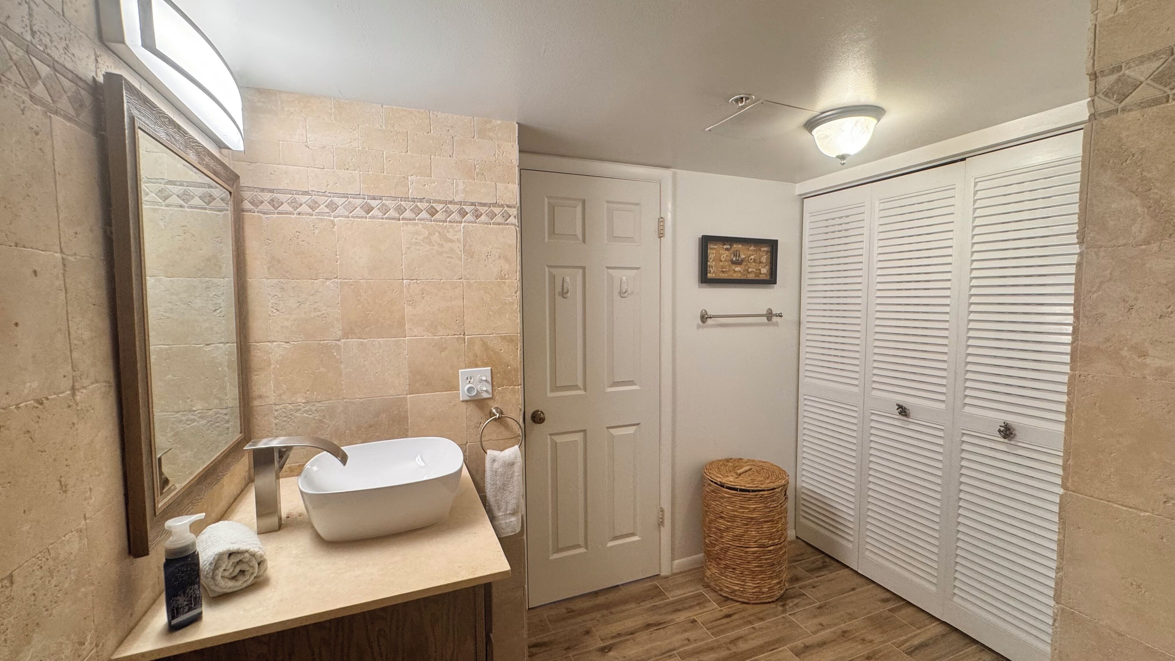 A bathroom with a large mirror, a white sink, a wooden vanity, a wicker basket, and a white door.