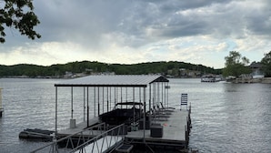Un muelle con una zona cubierta, un bote y vistas a un lago con una colina boscosa al fondo.