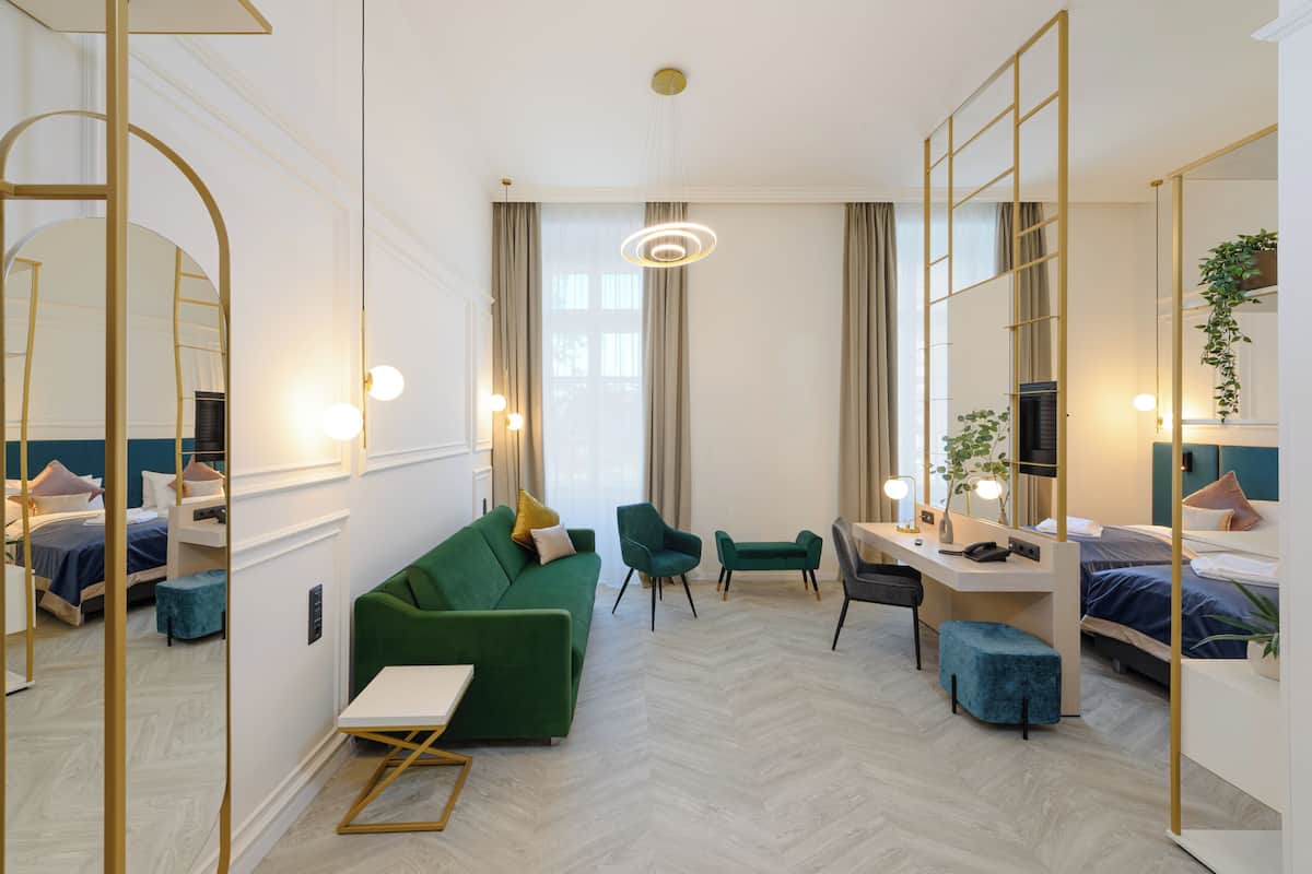 A hotel room with a green sofa, a desk with a computer, a chair, a bed, and a large mirror.