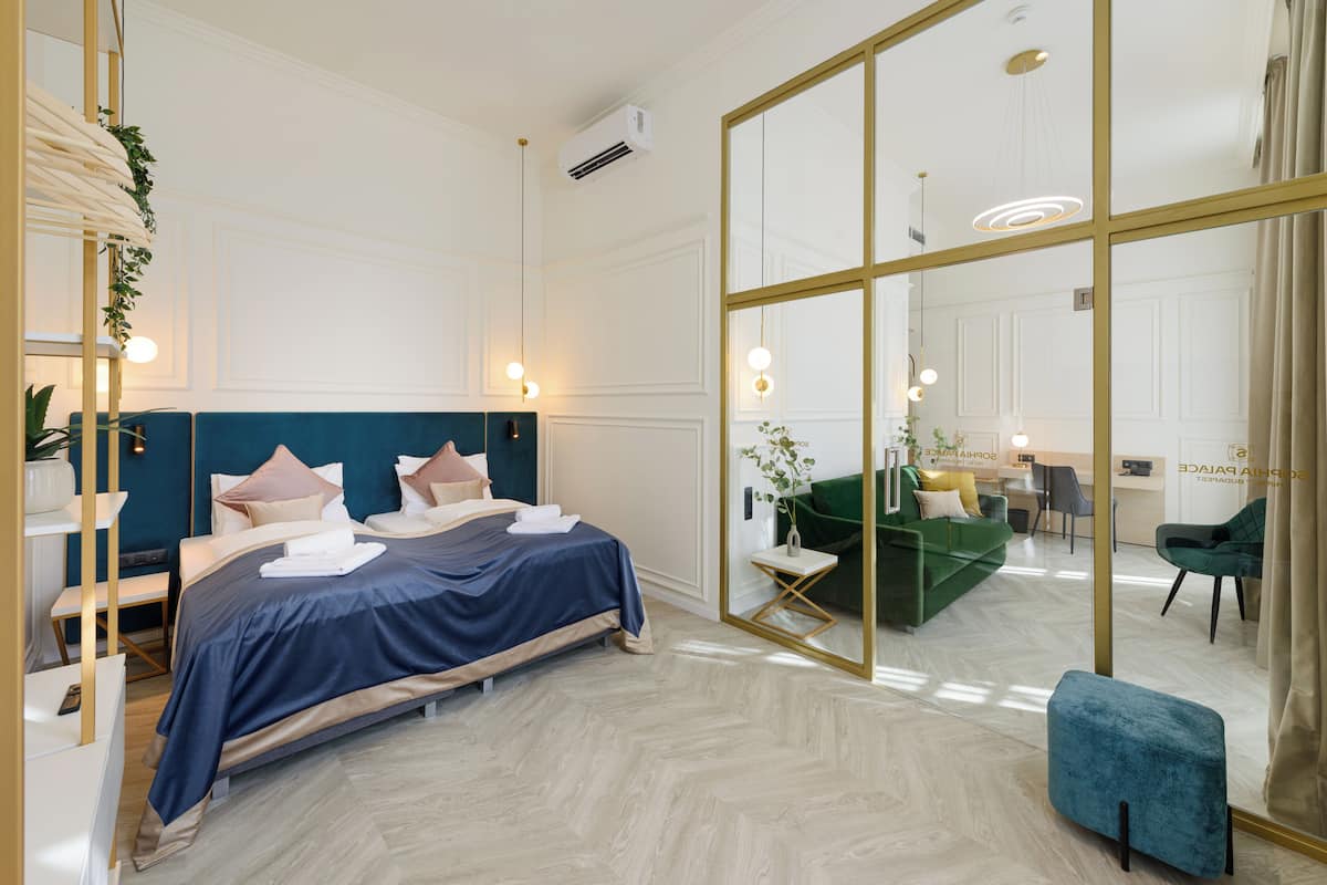 A modern hotel room with a large bed, a sitting area with a green sofa, and a mirrored wall.