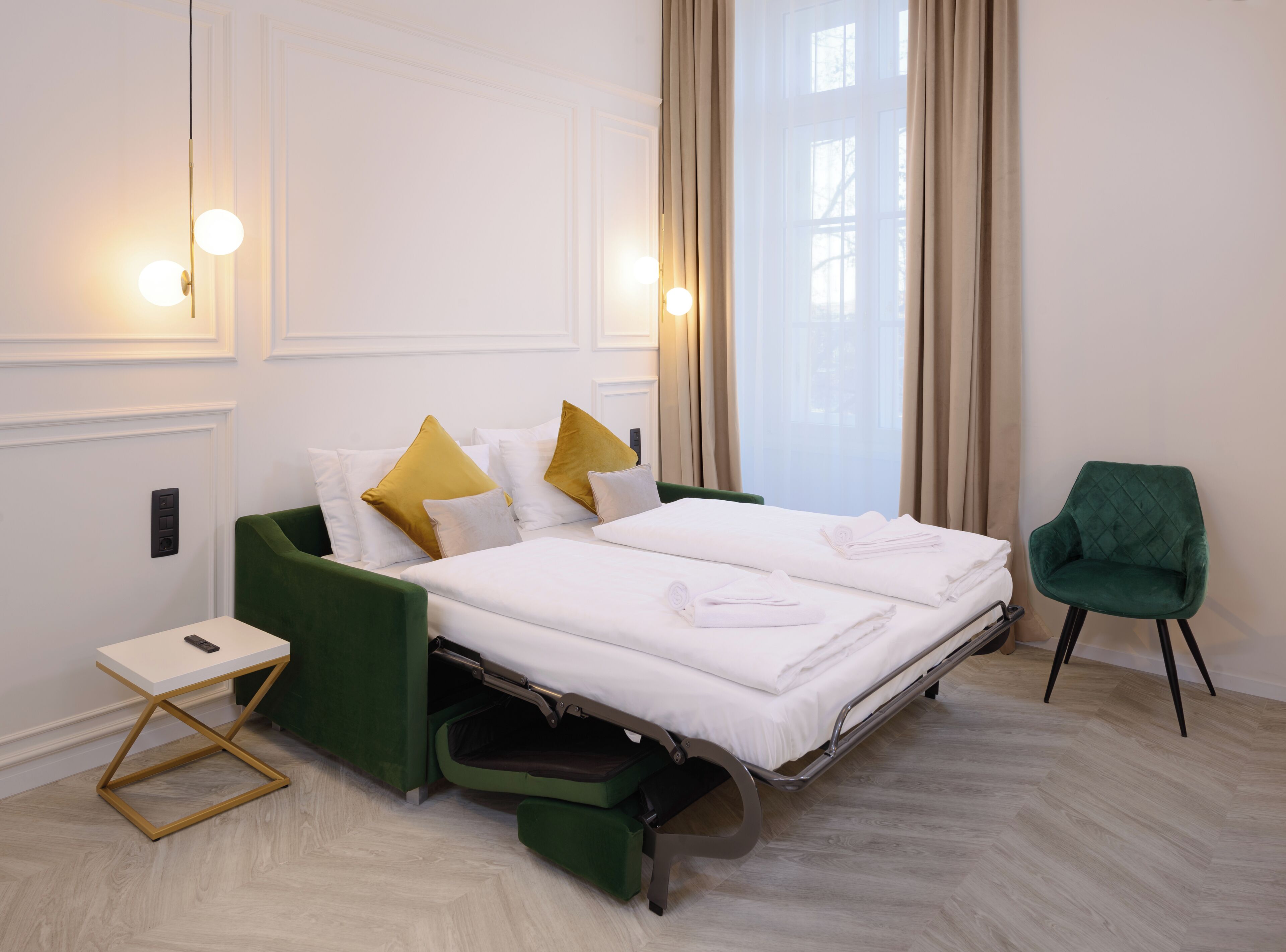 Een hotelkamer met een bed, een groene stoel, een tafeltje met een telefoon en een raam met gordijnen.