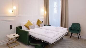 Een hotelkamer met een bed, een groene stoel, een tafeltje met een telefoon en een raam met gordijnen.