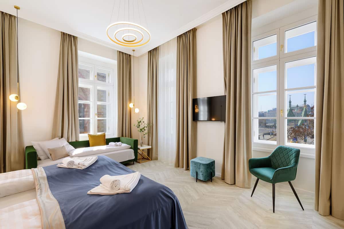 A hotel room with a bed, a green armchair, a small table, and a TV mounted on the wall.