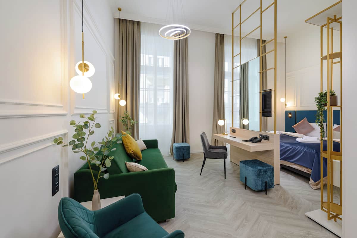 A modern hotel room with a green sofa, a desk, a bed, and a large mirror.