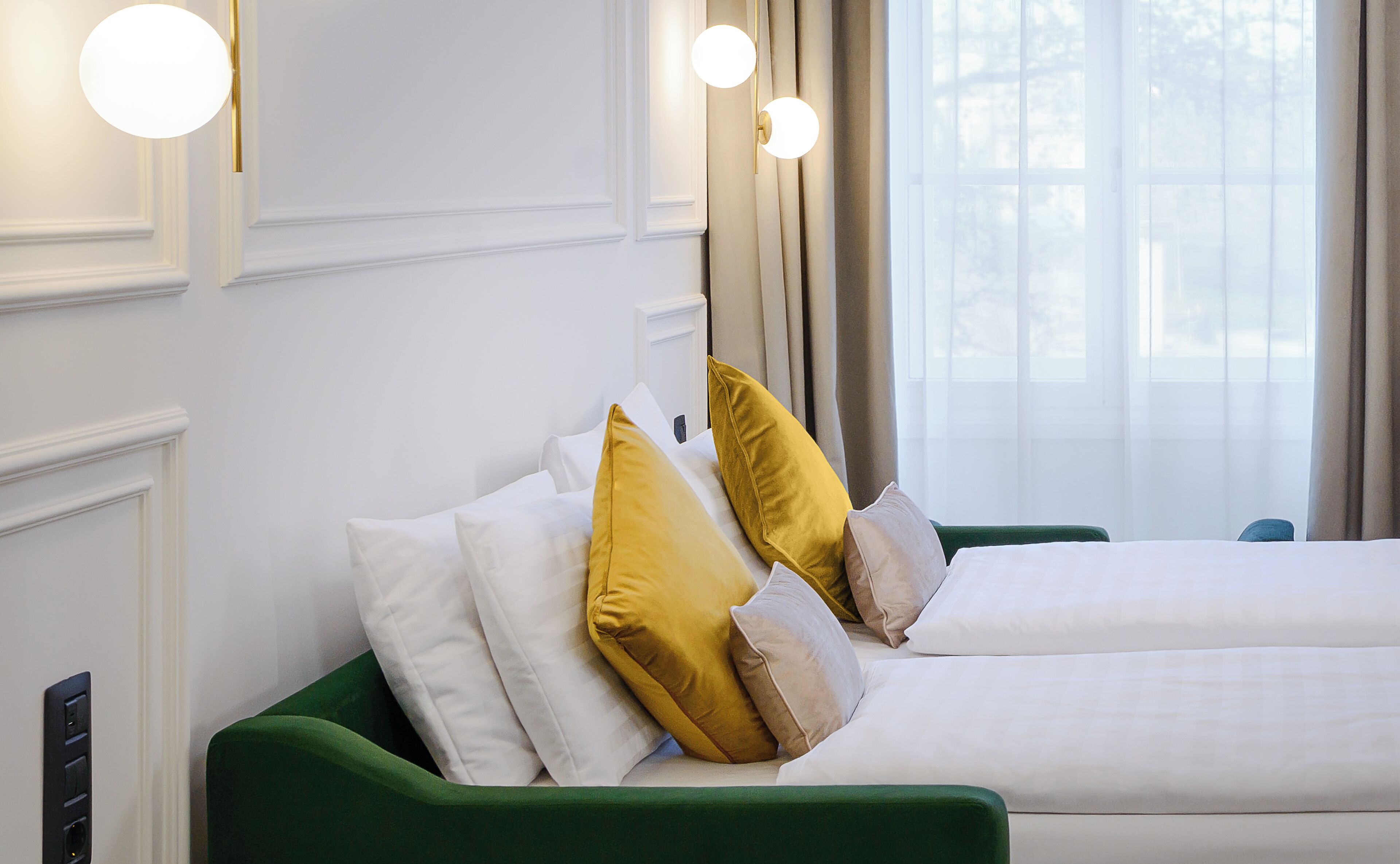 A hotel room with two beds, a green headboard, and a window with curtains.