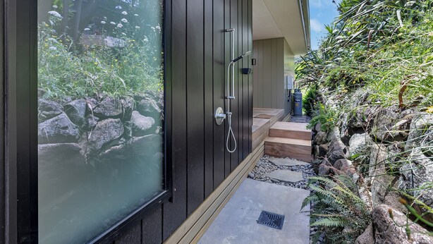 Uma casa de banho moderna com cabine de vidro, área de chuveiro e um caminho de pedra que leva a um deck de madeira.