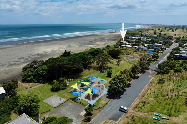 Vista aérea de uma área costeira com praia, estrada e parque com toldos azuis.