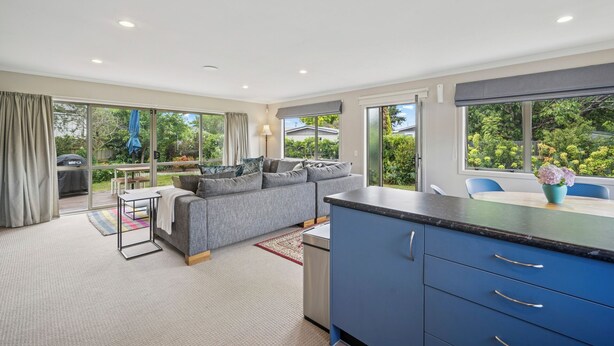Eine moderne Küche mit blauer Arbeitsplatte und Schränken, ein graues Sofa und ein Essbereich mit Tisch und Stühlen.