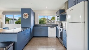Eine moderne Küche mit blauen Schränken, einem weißen Kühlschrank und einem Fenster mit Blick auf die Nachbarschaft.