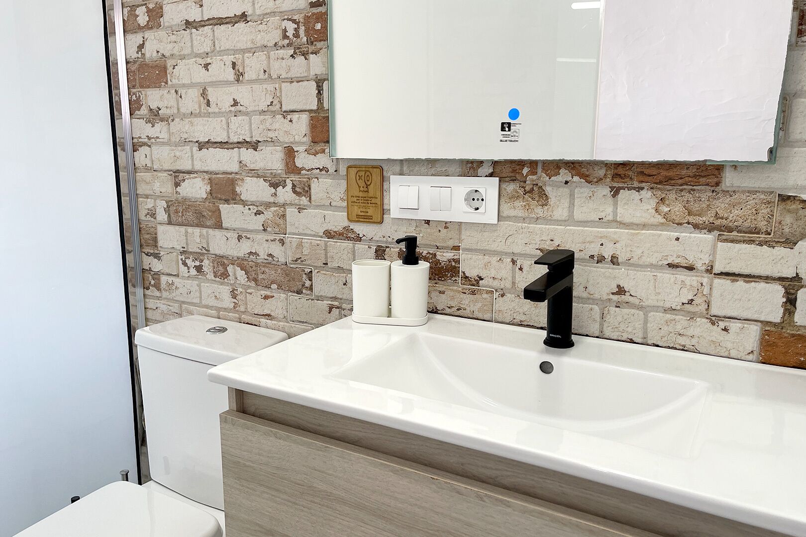 A bathroom with a white sink, black faucet, and a brick-patterned wall.