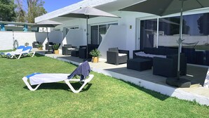 Un'area lounge esterna moderna con lettini e mobili in vimini sotto grandi ombrelloni.