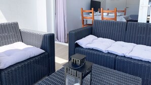 Un balcone con mobili in vimini, un tavolino e vista su una stanza con un letto e un tavolo da pranzo.