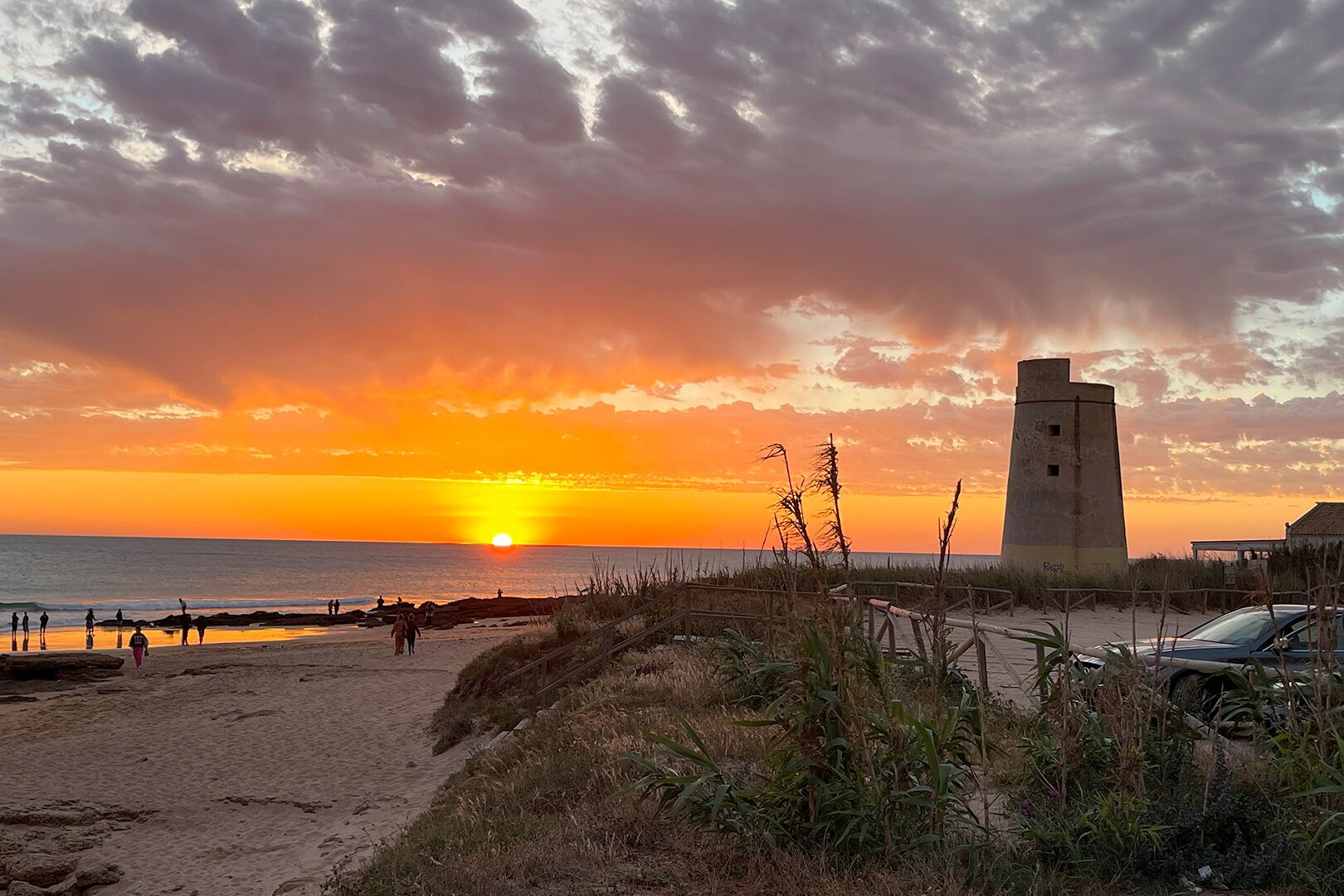 Una playa con una torre, dunas de arena y un atardecer.