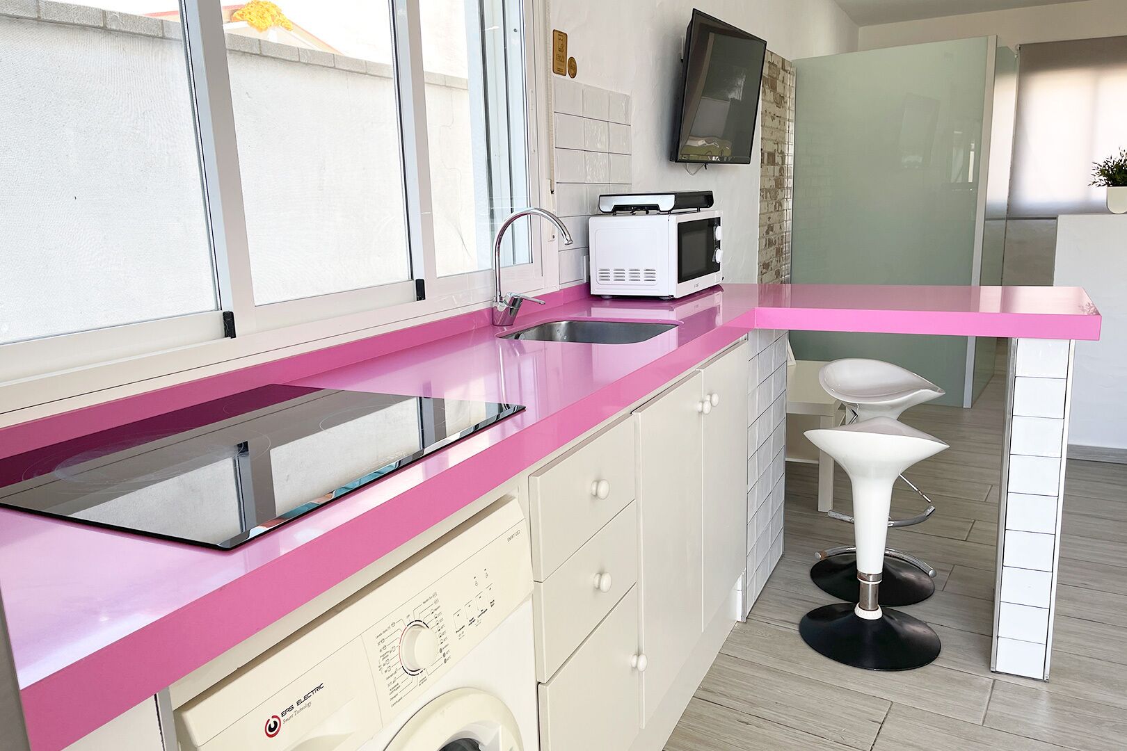 Cuina moderna amb taulell rosa, una rentadora, un microones i un rentaplat.