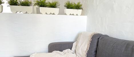 A gray sofa with a beige throw blanket and a white wall with three white planters with green plants.