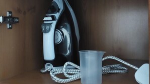 A compact iron with a cord and a plastic cup on a wooden surface. - Couples/business/family- Wifi- Parking- Sleeps 2 (Coventry)