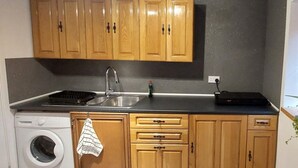 A compact kitchen with wooden cabinets, a washing machine, and a countertop with a sink and a small appliance. - Couples/business/family- Wifi- Parking- Sleeps 2 (Coventry)