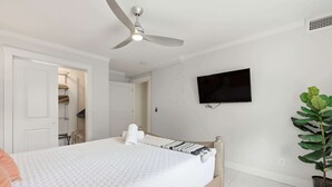 Een slaapkamer met een bed, een plafondventilator, een aan de muur bevestigde televisie en een potplant.