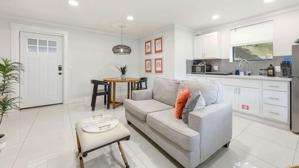 Een moderne woonkamer met een grijze bank, een klein rond tafeltje en een witte fauteuil. In de achtergrond is een keuken met witte kastjes en een zwart aanrecht te zien.