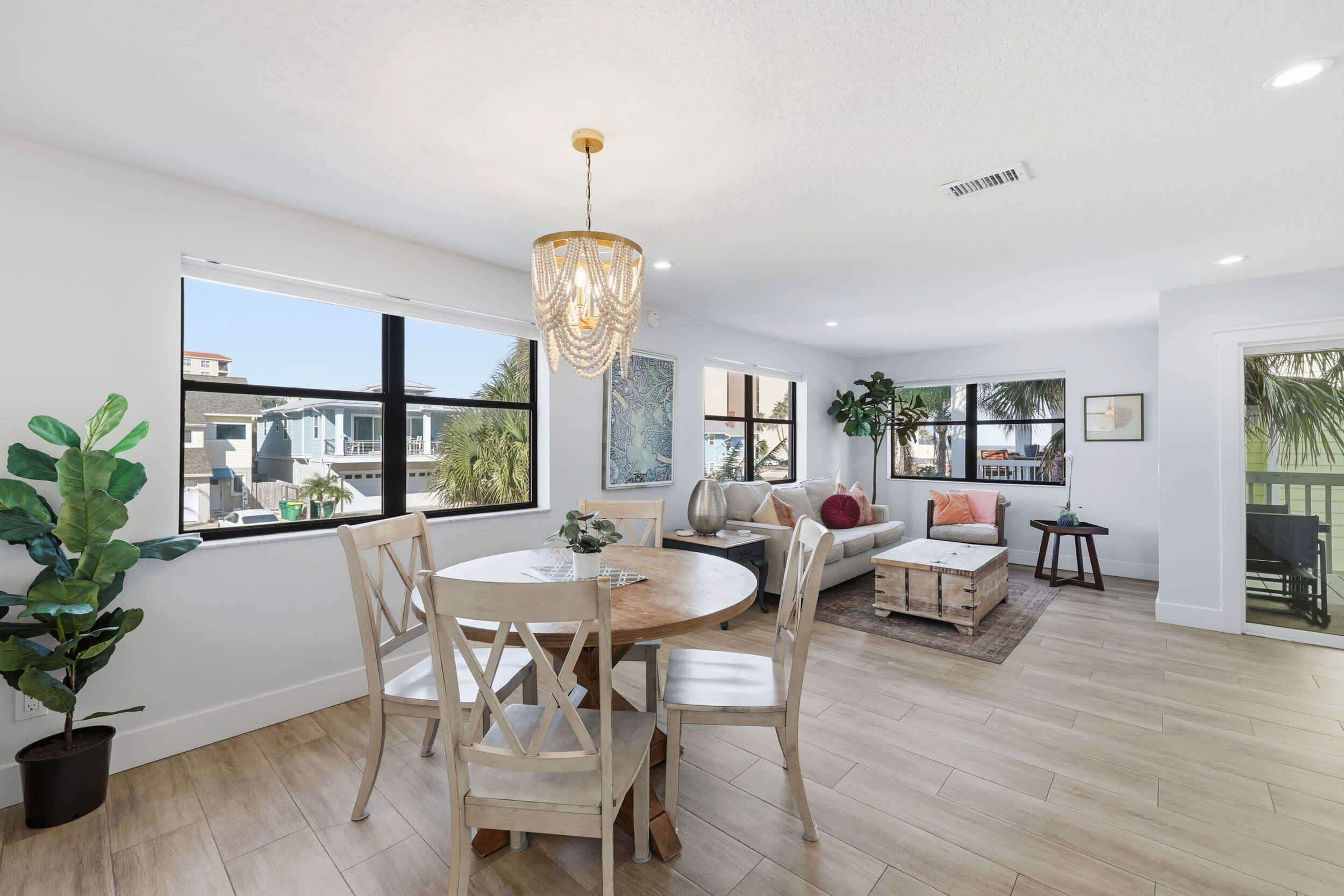 Uma sala de estar espaçosa com uma mesa de jantar redonda de madeira, um candelabro e grandes janelas com vista para a cidade.