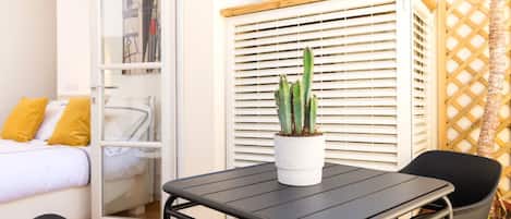 Una stanza compatta con un letto, un tavolino, due sedie, un cactus in vaso e un pannello di legno a griglia.