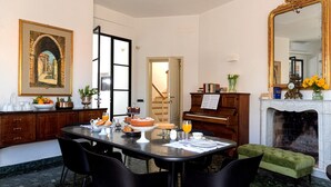 A dining area with a marble floor, a piano, a fireplace, and a painting of an archway. - LEOPOLDO ROOMS (Cagliari)