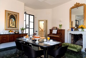Un comedor con suelo de mármol, un piano, una chimenea y un cuadro de un arco.