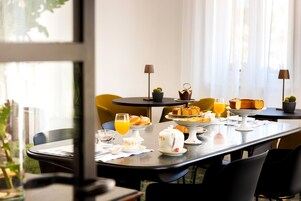 Un desayuno con una mesa preparada para dos, que incluye varios pasteles, una tetera y un vaso de jugo de naranja.