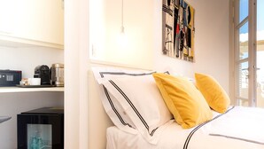 A neatly made bed with white bedding and two pillows, a coffee machine, and a small black cabinet on a white wall. - LEOPOLDO ROOMS (Cagliari)