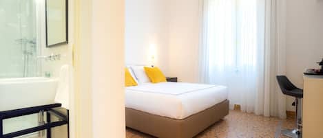 A hotel room with a bed, a desk, a chair, a bathroom with a bathtub, and a window with curtains.