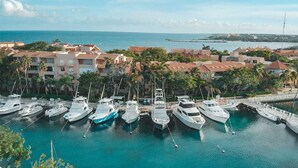 A marina with several yachts docked, surrounded by residential buildings and palm trees. - Departamento cerca del mar 103 (Puerto Aventuras)