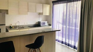 A modern kitchen with a built-in microwave, a sink, and two bar stools. - Departamento cerca del mar 103 (Puerto Aventuras)
