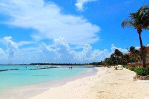 Une plage avec une eau turquoise et limpide, des palmiers et quelques personnes au loin.