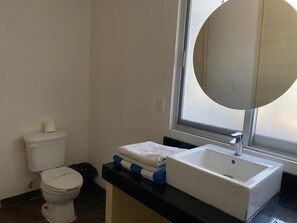 A bathroom with a toilet, a sink, a mirror, and a window. - Departamento cerca del mar 103 (Puerto Aventuras)
